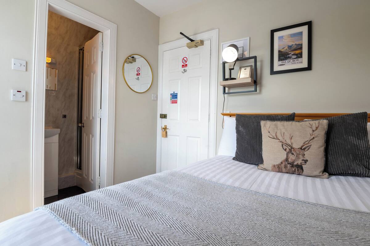 A bedroom with a bed, a bedside table, a mirror, a framed picture, and a door with a sign.
