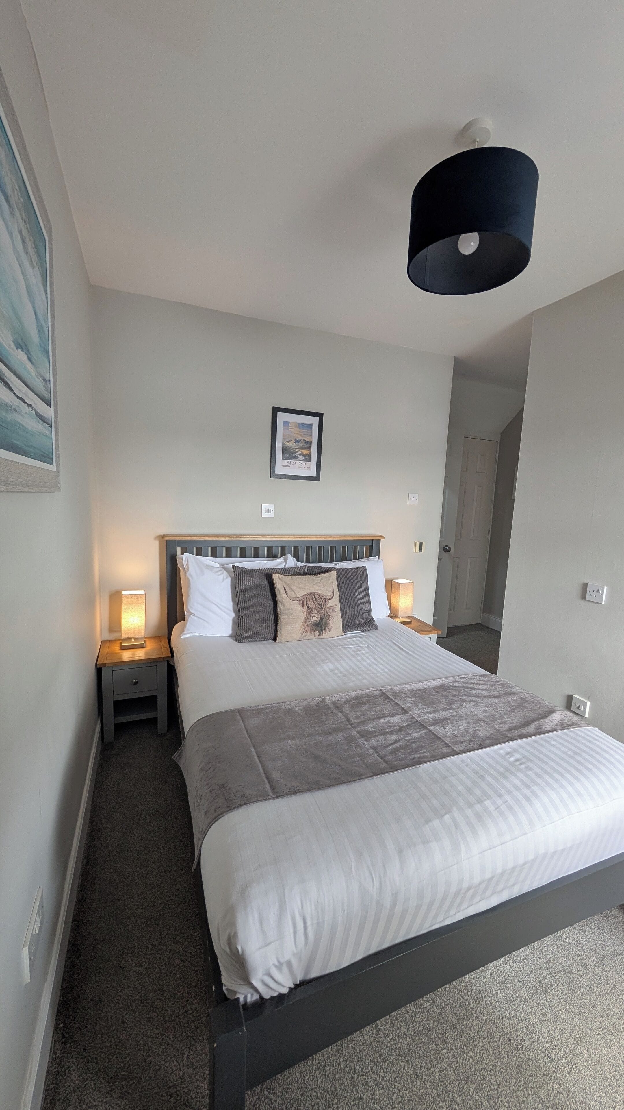 A neatly arranged bedroom with a bed, bedside lamps, a framed picture on the wall, and a ceiling light fixture.