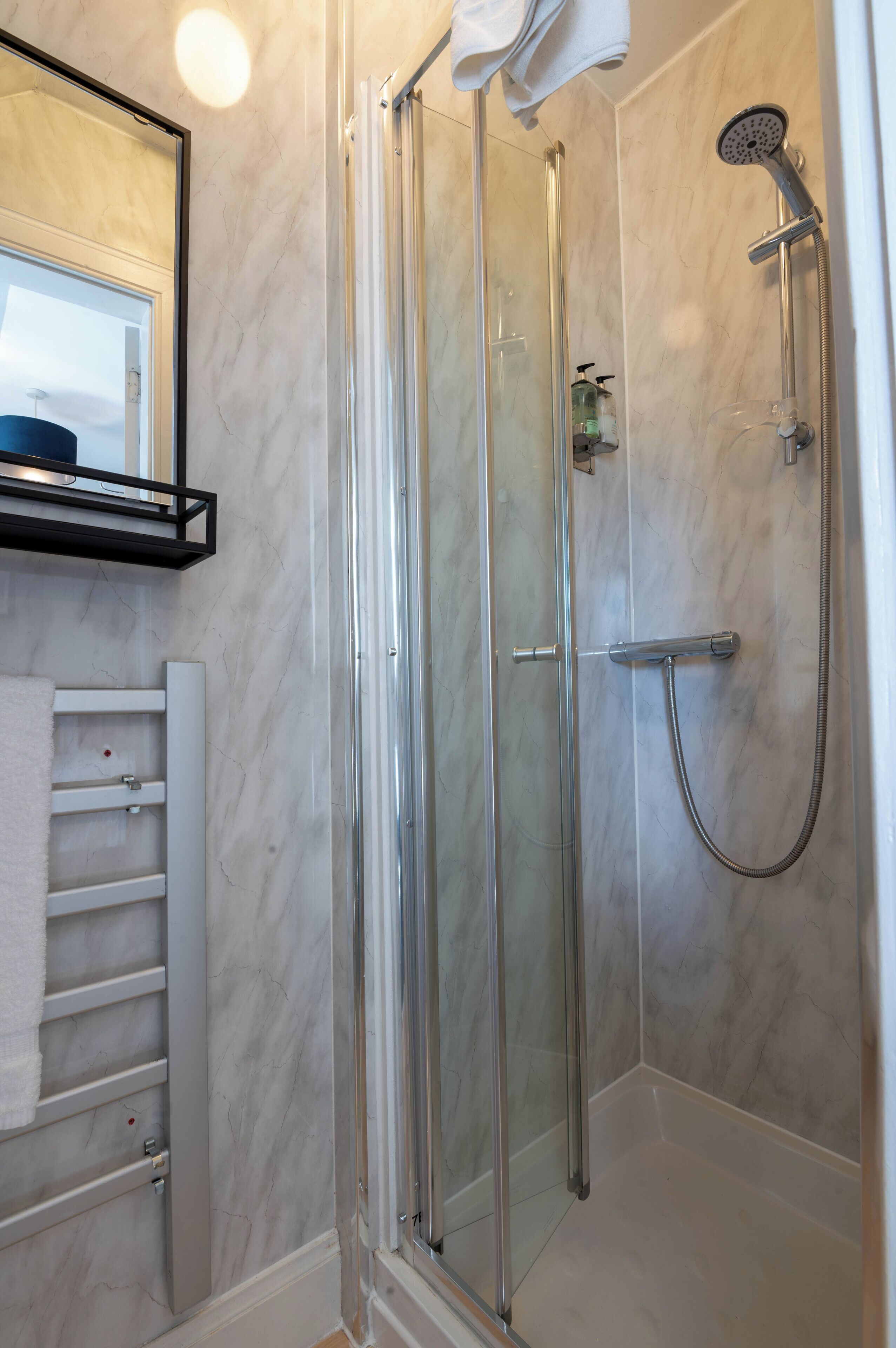 A glass-enclosed shower with a handheld showerhead and a towel rack.