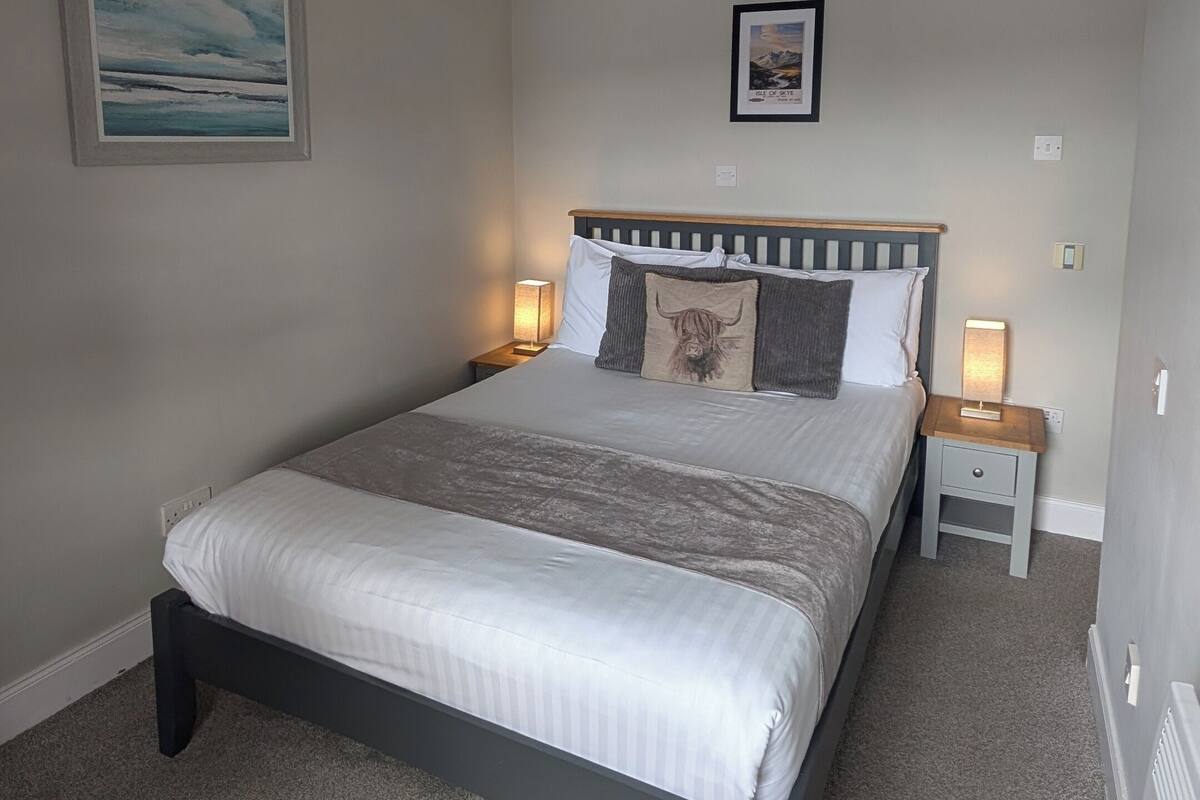 A bedroom with a bed, bedside lamps, a ceiling light, and a framed picture on the wall.