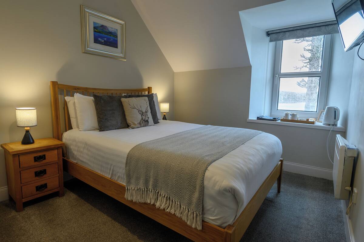 A neatly made bed with a wooden headboard, a bedside lamp, and a framed picture on the wall.