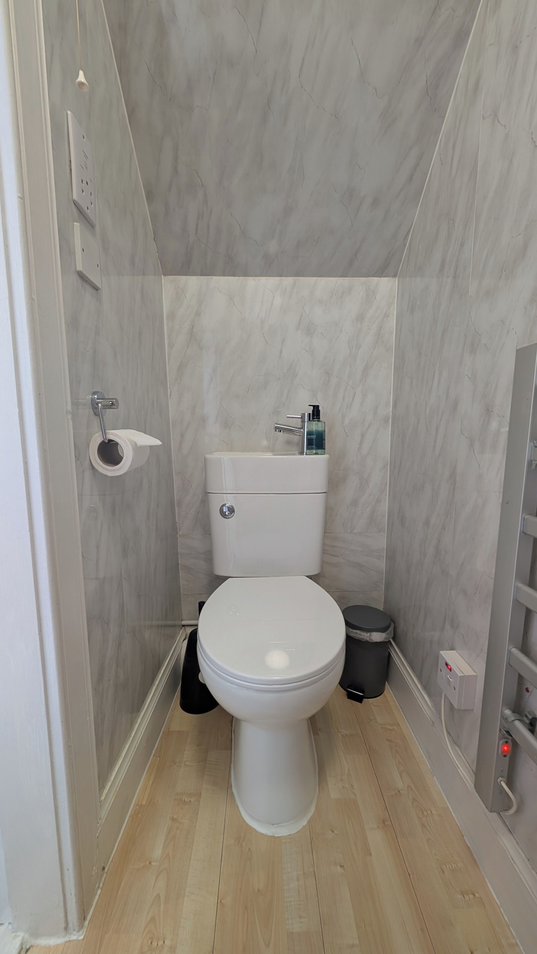 A compact bathroom with a toilet, a hand dryer, and a trash bin.