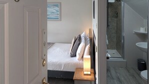 Ett sovrum med en säng, ett sängbord och ett litet bord med en lampa. Det finns också ett badrum med ett handfat och en spegel.