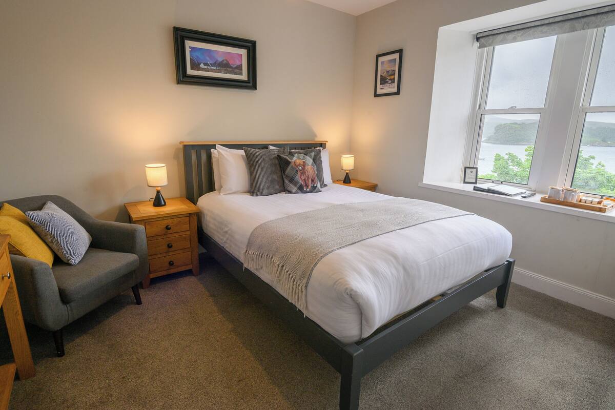 A bedroom with a bed, bedside tables, a chair, and a window with a view.
