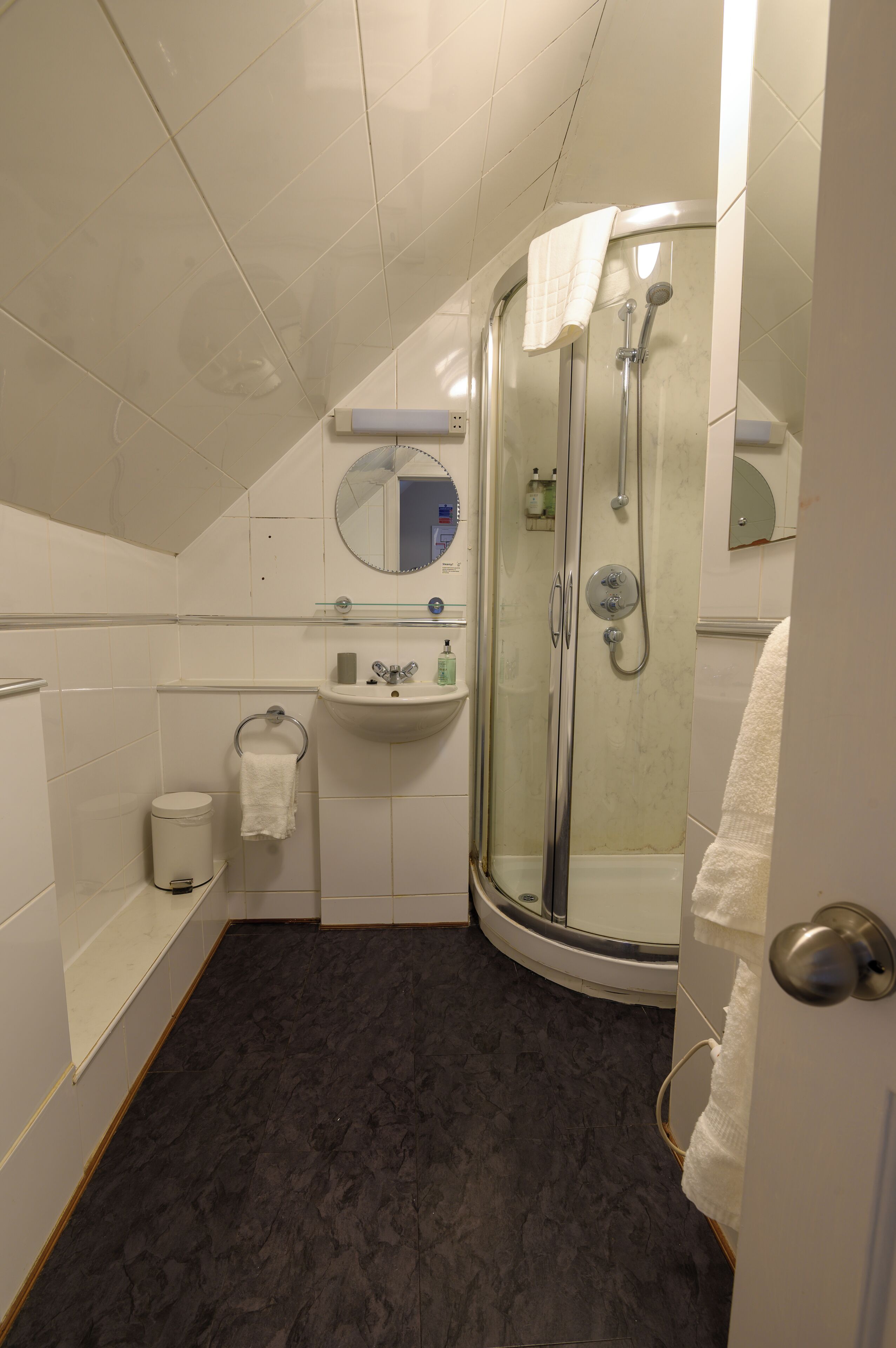 Un baño moderno con ducha de vidrio, lavamanos con espejo y un inodoro con toallero.