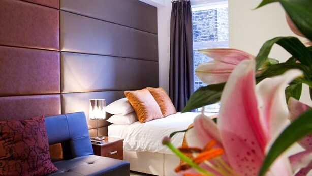 A modern hotel room with a large bed, a sofa, a nightstand, and a window with curtains. - City Inn Russell Square (London)