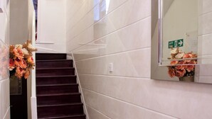 A hallway with a marble floor, a dark staircase, white walls, and a mirror with a floral arrangement. - City Inn Russell Square (London)