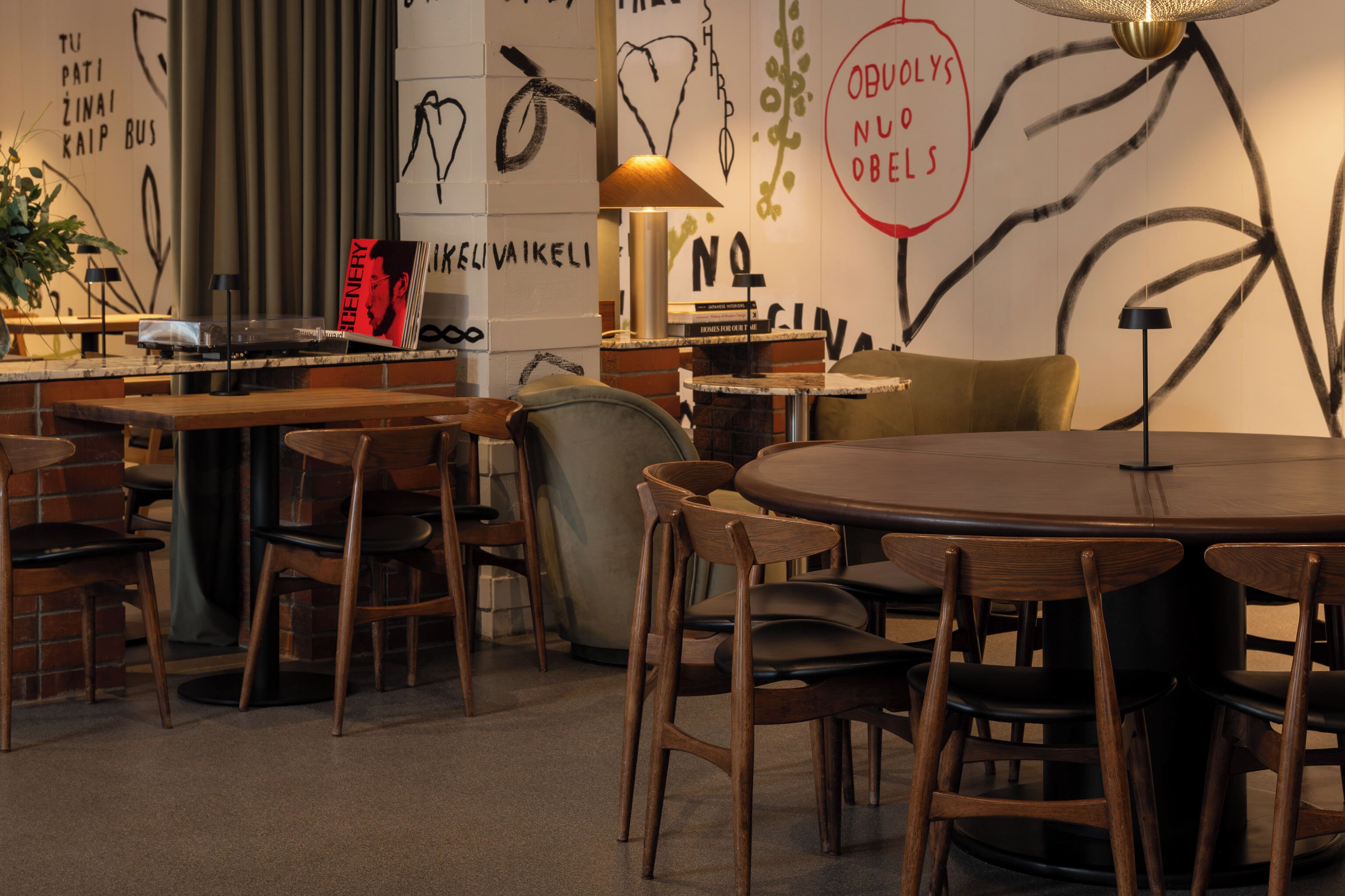 Un restaurant à l’ambiance chaleureuse, avec des tables et des chaises en bois, un comptoir doté d’une platine vinyle et des œuvres d’art accrochées aux murs.