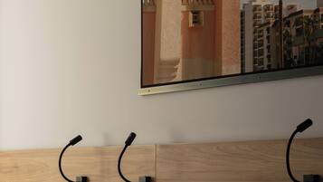 Habitación de hotel con cabecera de madera, dos camas con almohadas y un espejo en la pared que refleja un edificio y una palmera.