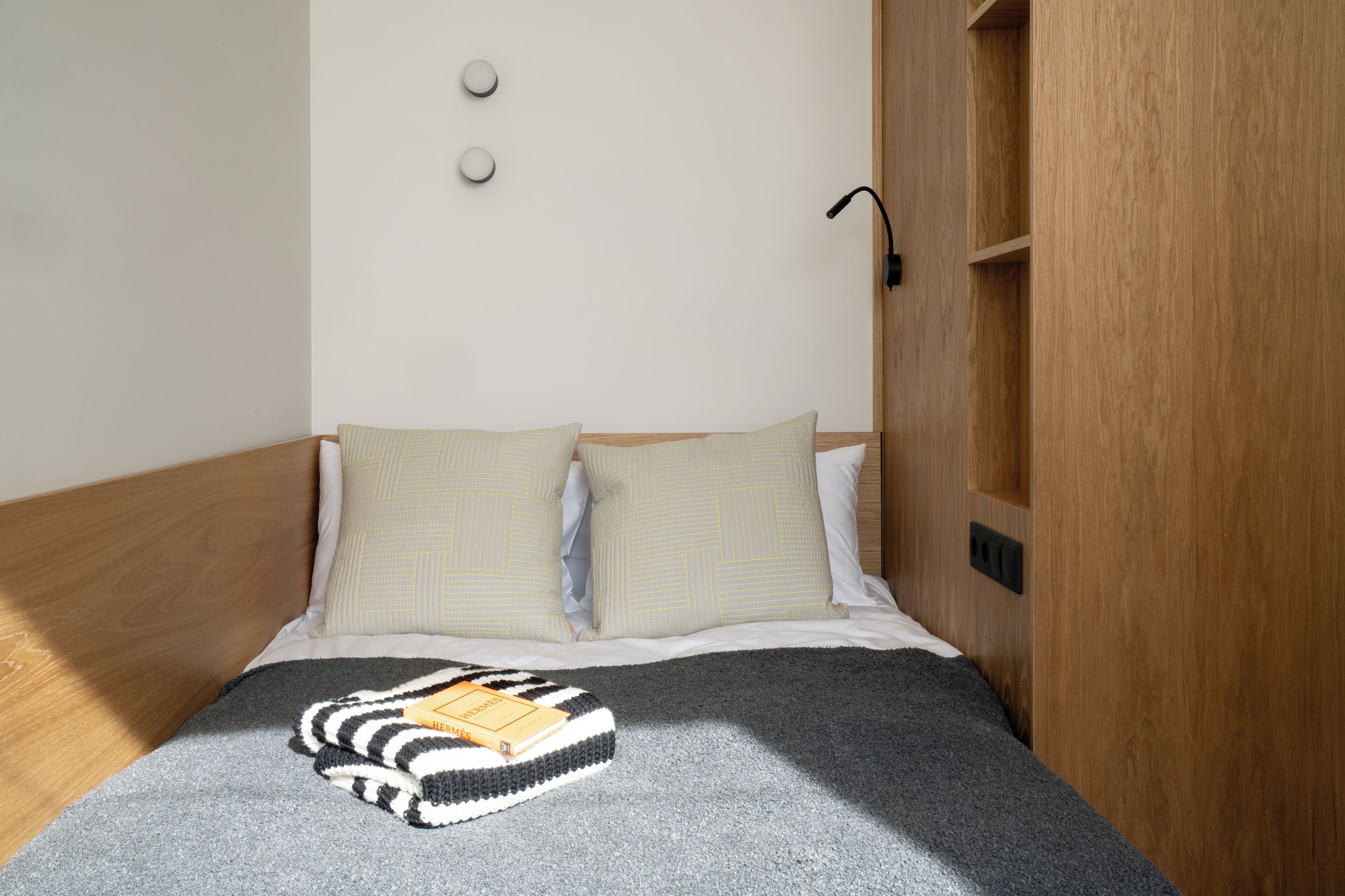 A neatly made bed with two pillows, a bedside lamp, and a book on a blanket.