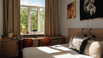 Habitación de hotel con cama, escritorio, silla, ventana con cortinas y obras de arte en las paredes.