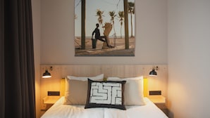 Habitació d'hotel amb un llit, una tauleta de nit, un quadre penjat a la paret i un coixí amb un disseny singular.