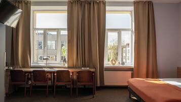 A hotel room with a bed, desk, chairs, and large windows with curtains.