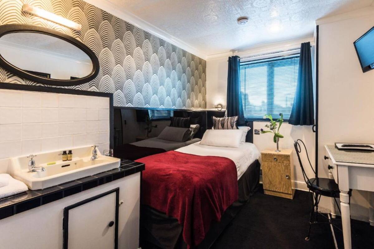A hotel room with a bed, a desk, a chair, a sink, and a mirror.
