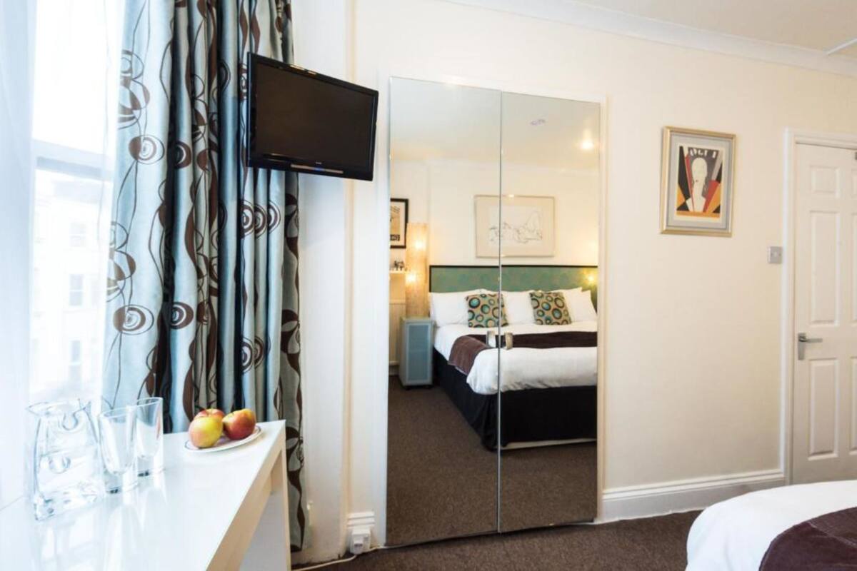 A hotel room with a bed, a TV mounted on the wall, a mirror, and a painting on the wall.