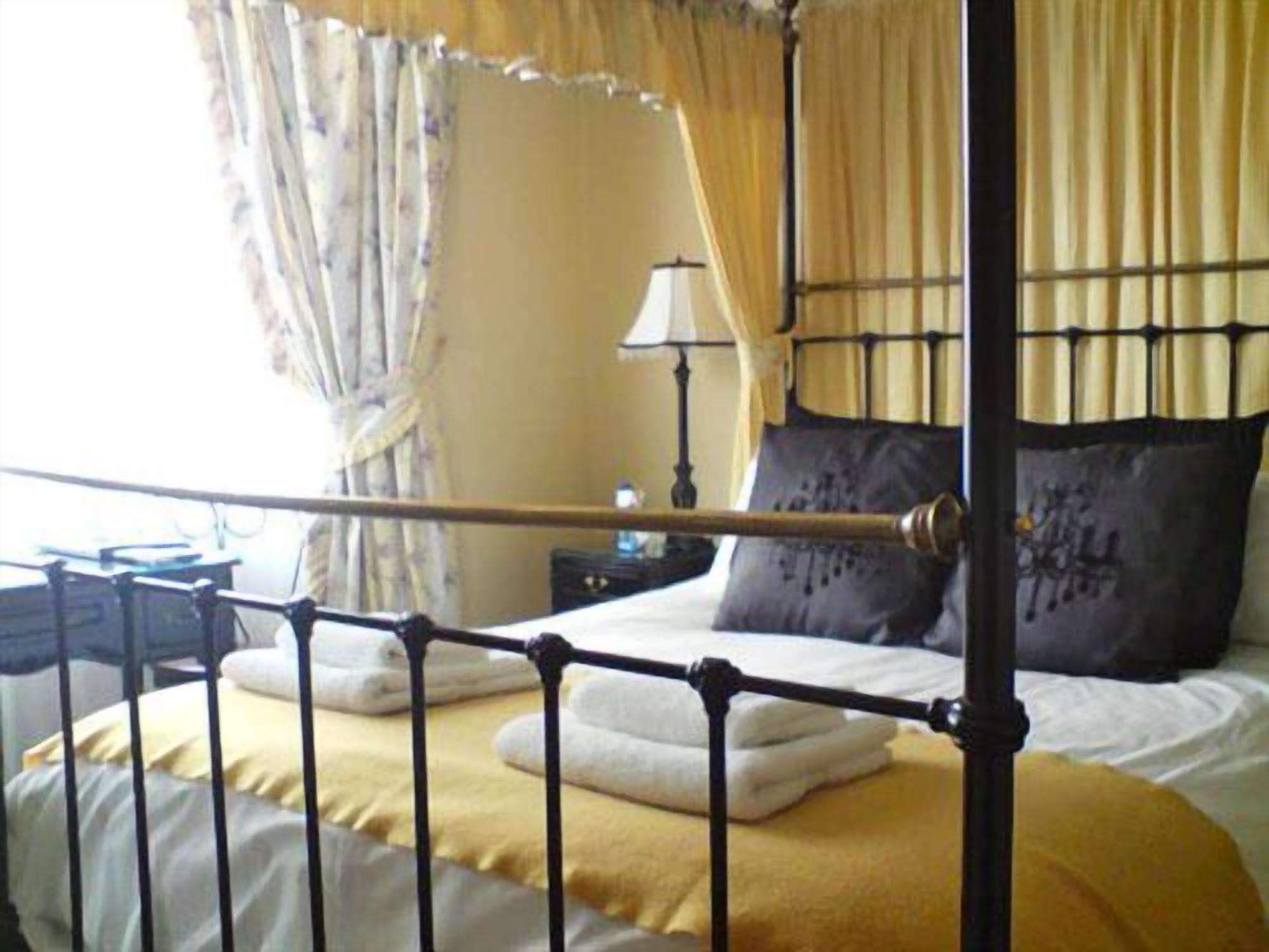 A four-poster bed with a metal frame, a bedside table with a lamp, and a window with curtains.