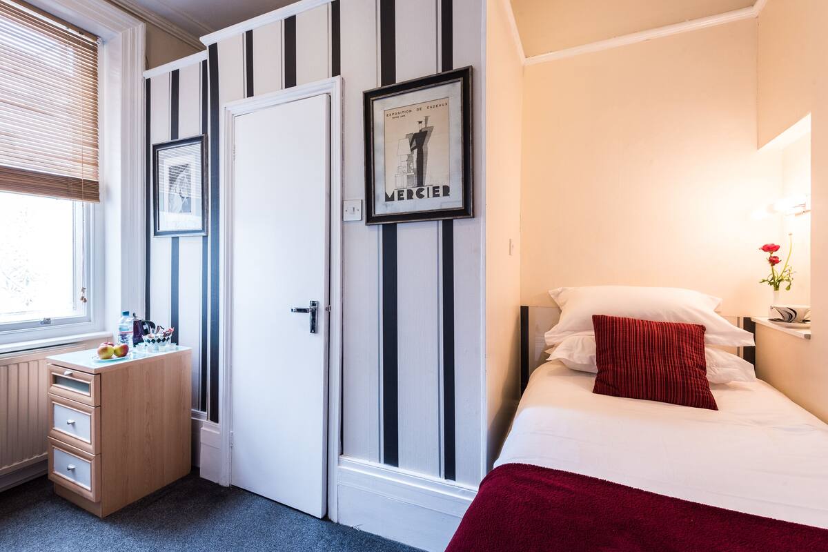 A bedroom with a bed, a dresser, a window with blinds, and a door with a striped pattern.