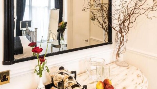 A hotel room with a marble dresser, a large mirror, and a vase with red flowers. - Paskins Townhouse (Brighton)