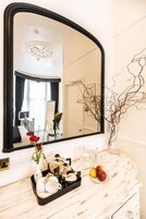Una habitación de hotel con un tocador de mármol, un espejo grande y un jarrón con flores rojas.