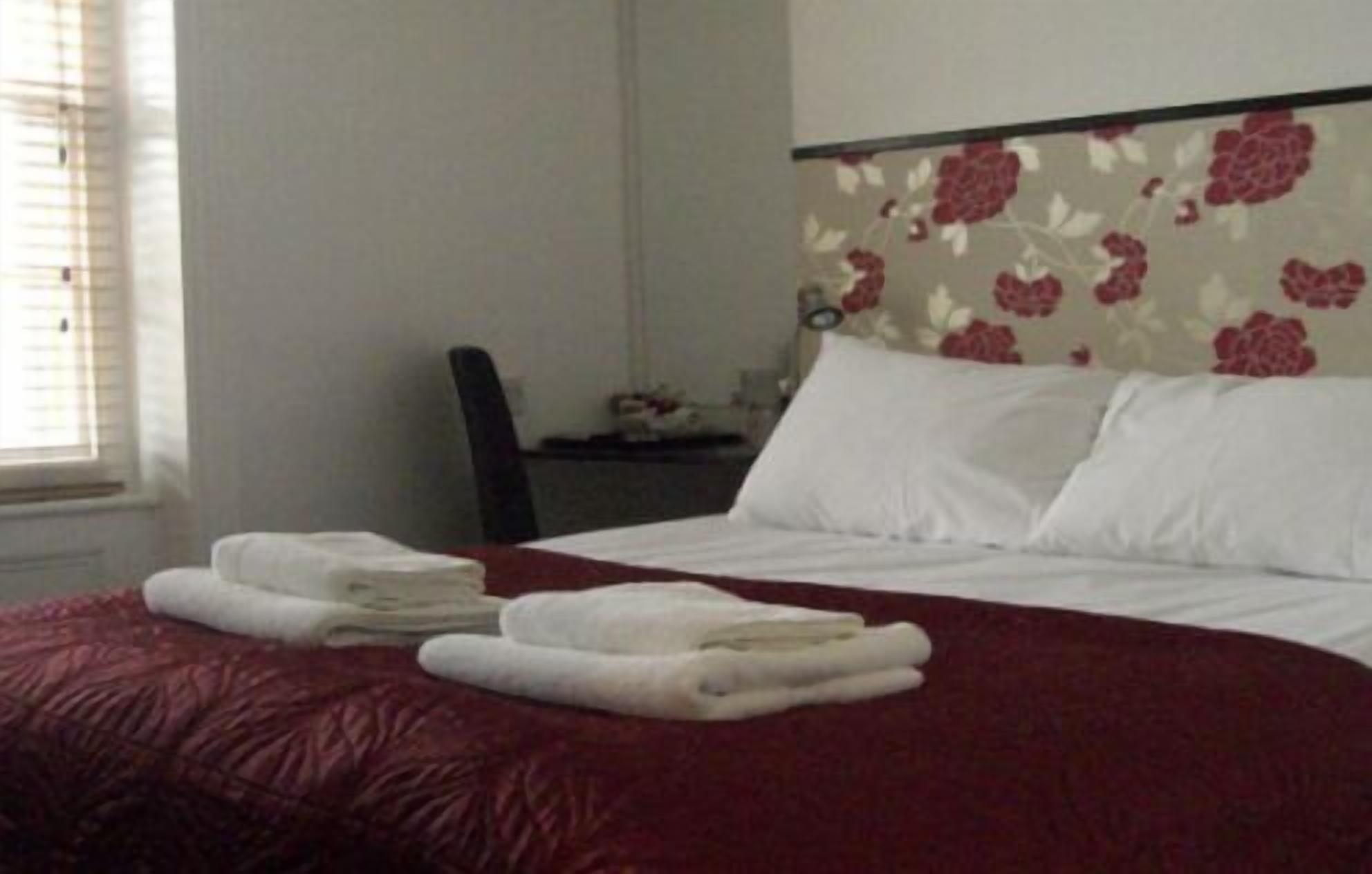A hotel room with a bed, two pillows, a chair, and a desk with a lamp.
