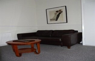Una sala de estar con un sofá de cuero oscuro, una mesa de centro de madera y un cuadro abstracto enmarcado en la pared.