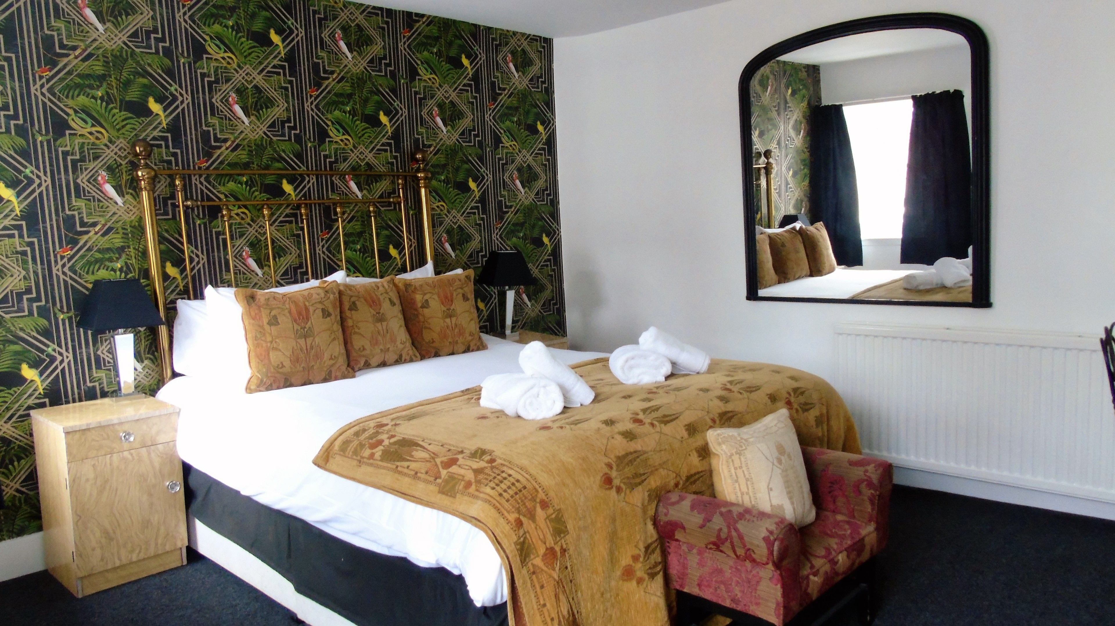 Una habitación de hotel con cama, mesita de noche, espejo y silla.