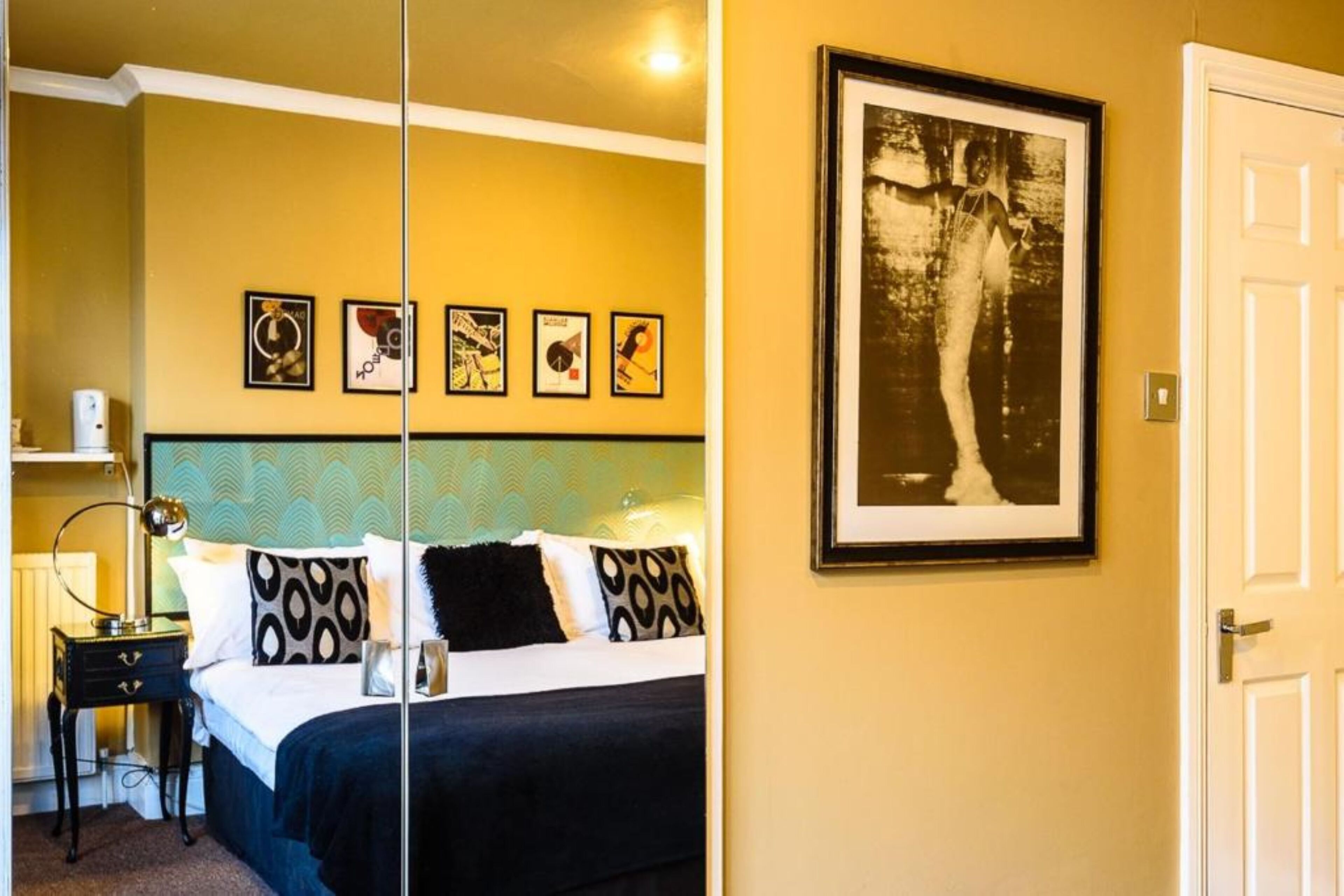 A bedroom with a bed, bedside table, lamp, and a wall with framed pictures.
