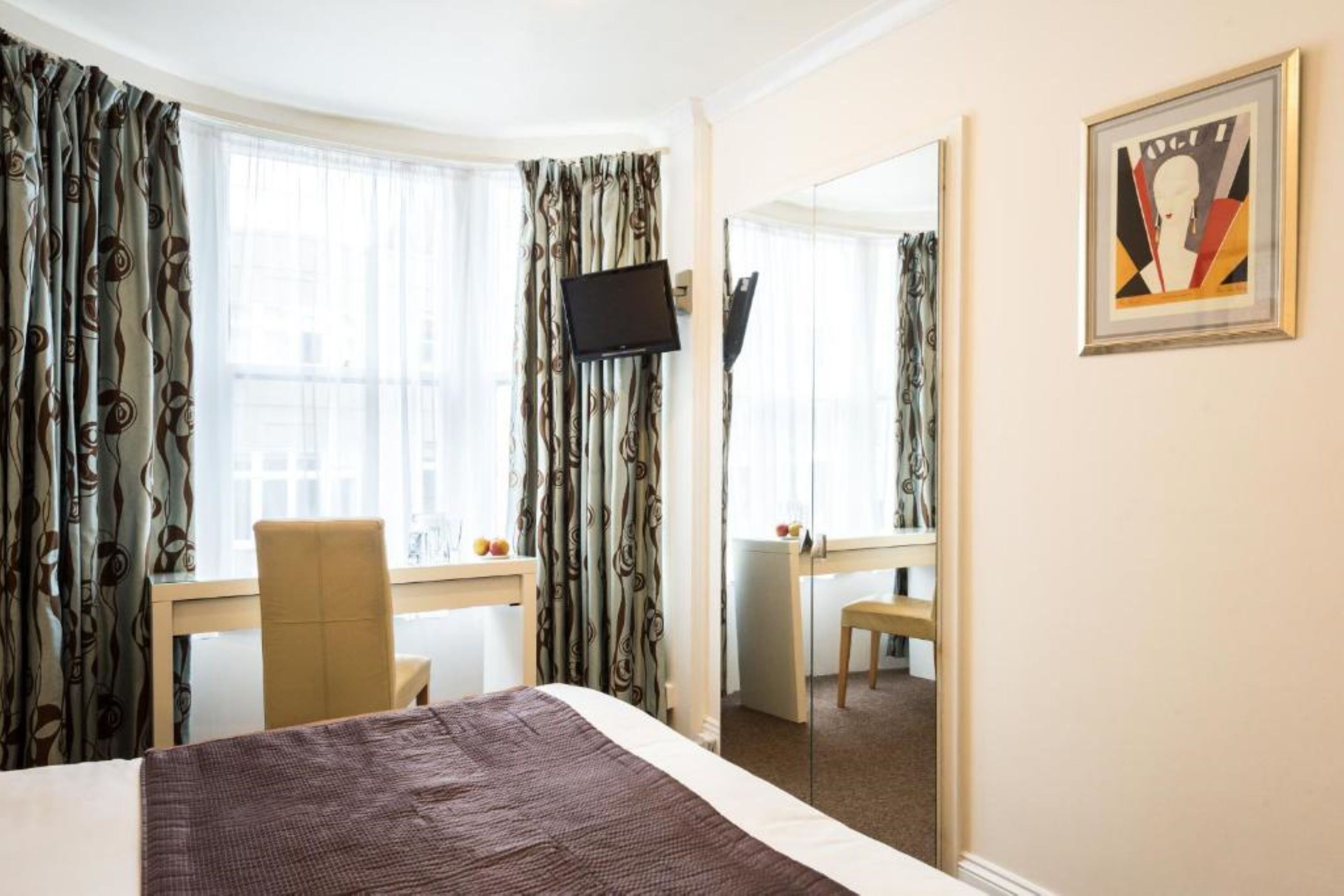 A hotel room with a bed, a desk, a chair, a television, and a mirror.