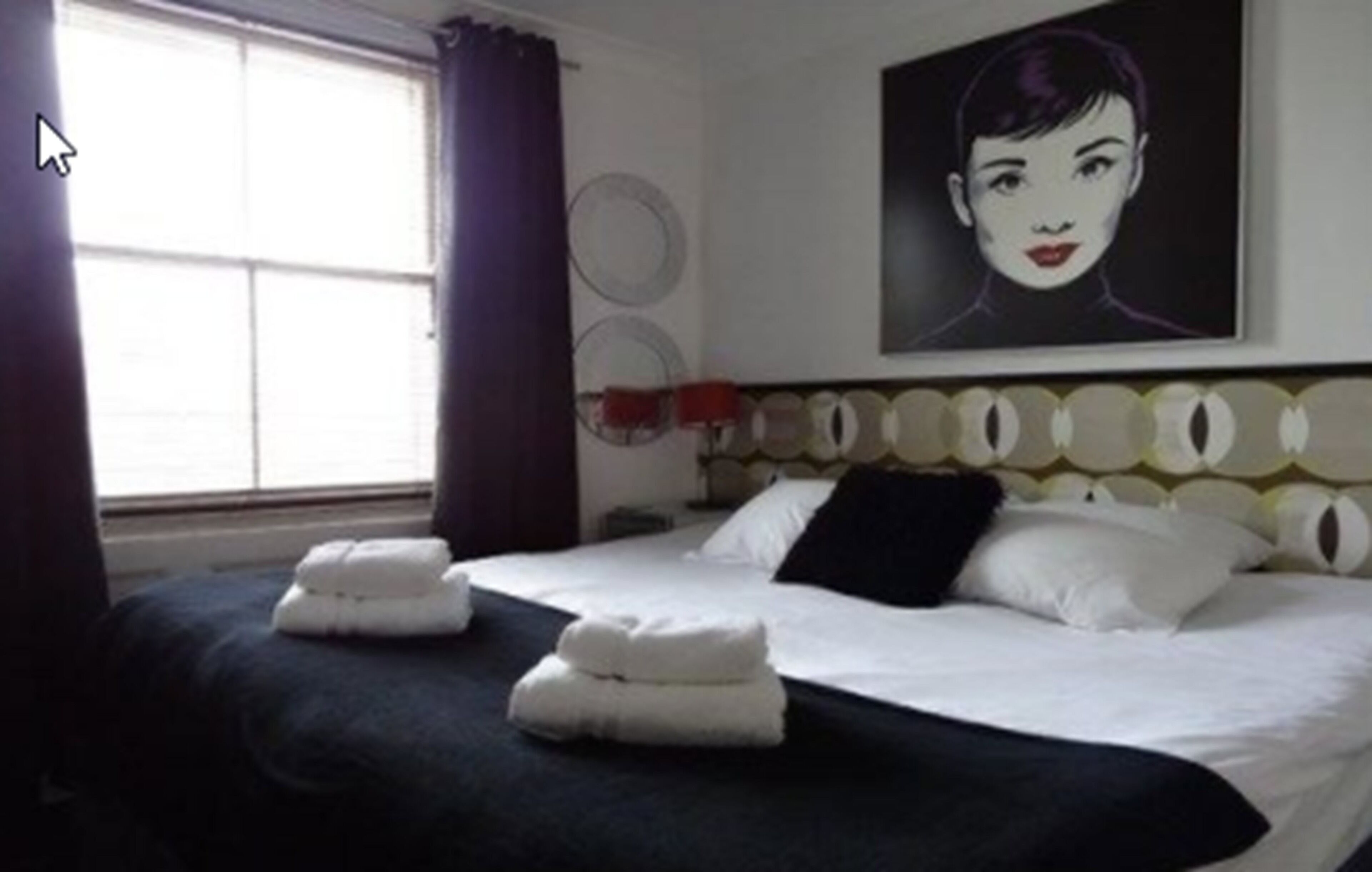 A hotel room with a bed, pillows, and a painting on the wall.