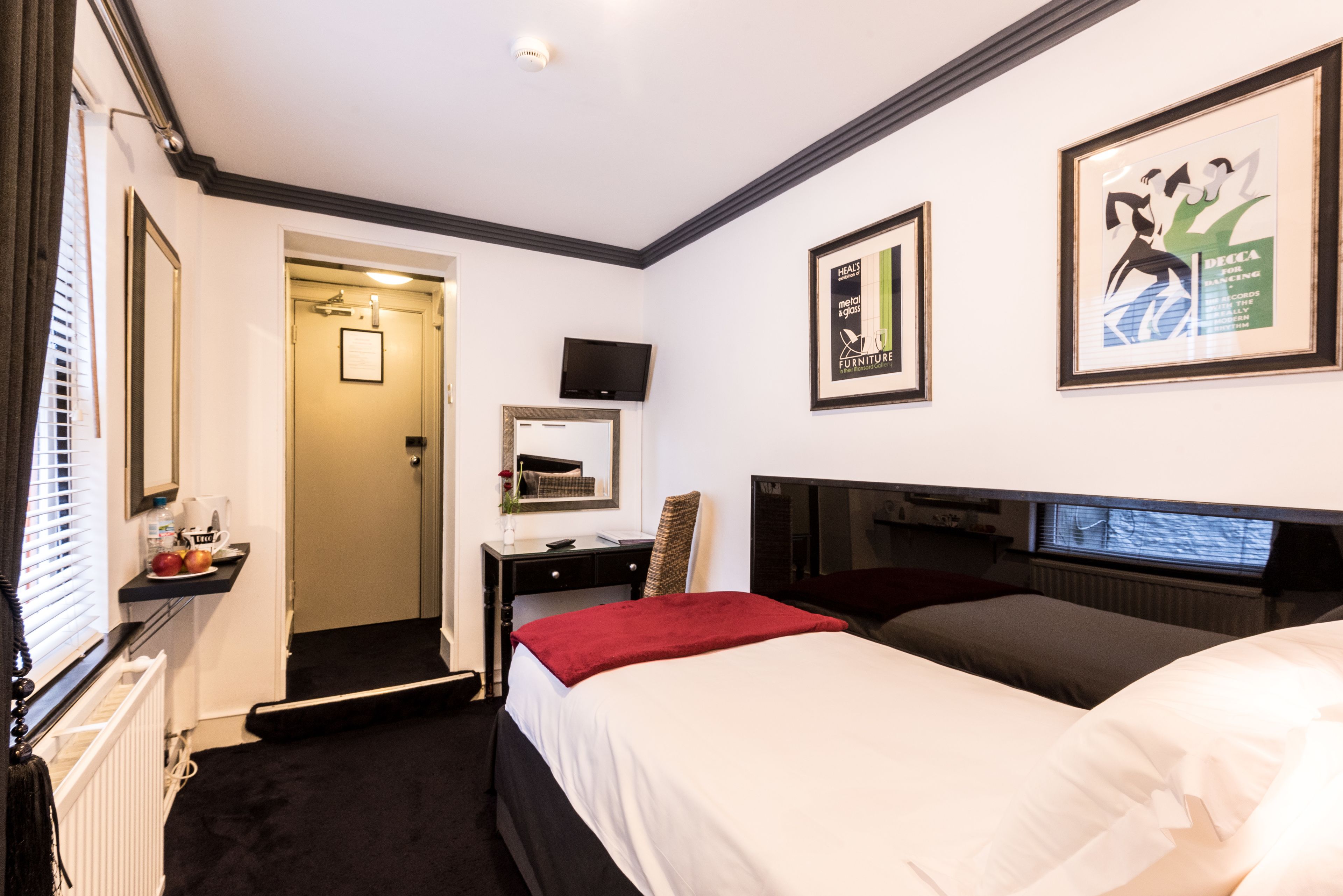 Habitación de hotel con cama, escritorio, silla, televisión y cuadros en las paredes.