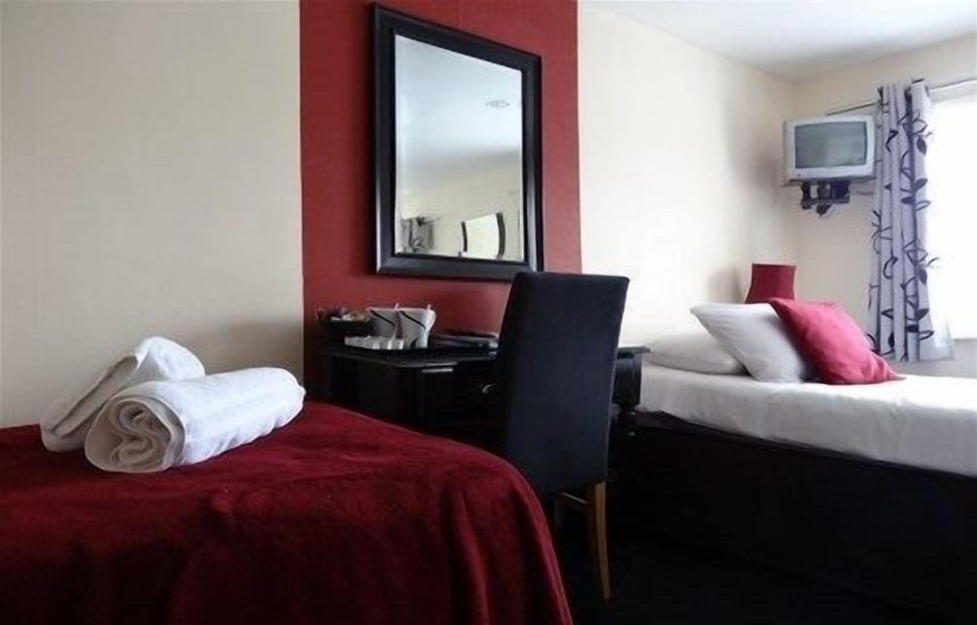 A hotel room with two beds, a desk, a chair, a TV, and a window with curtains.