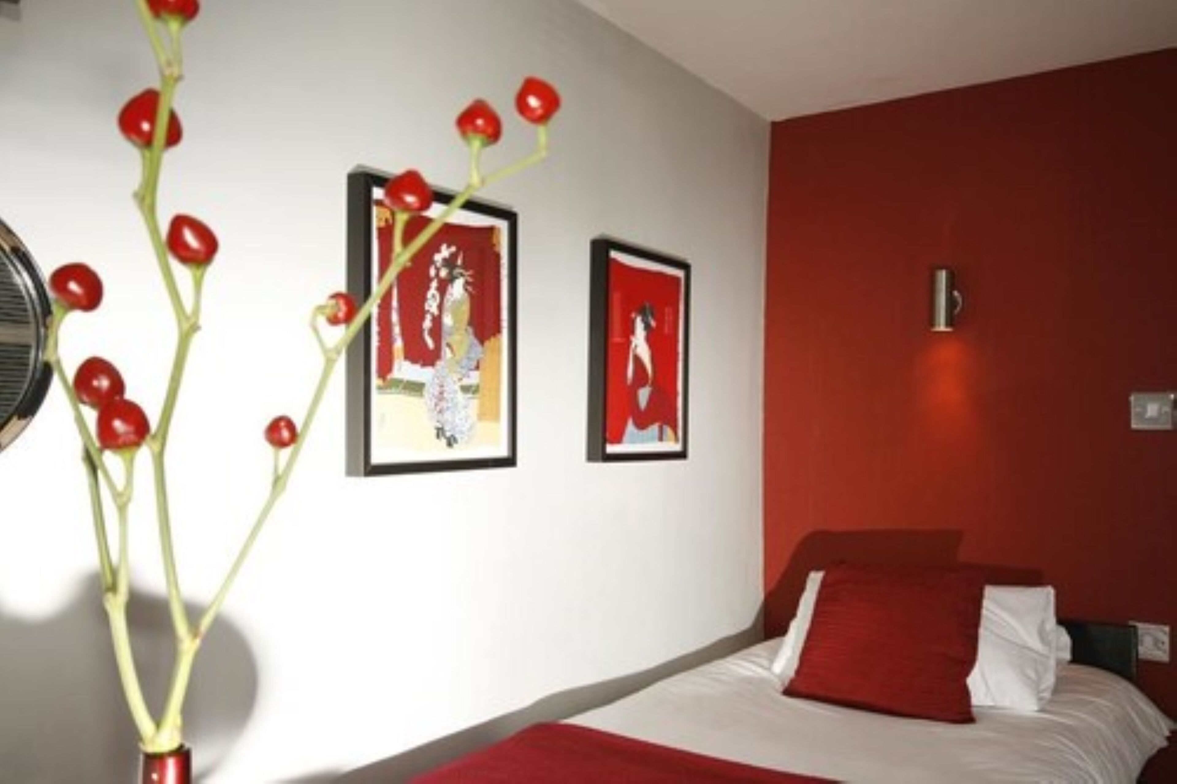 A hotel room with a bed, a wall-mounted light, and two framed pictures.