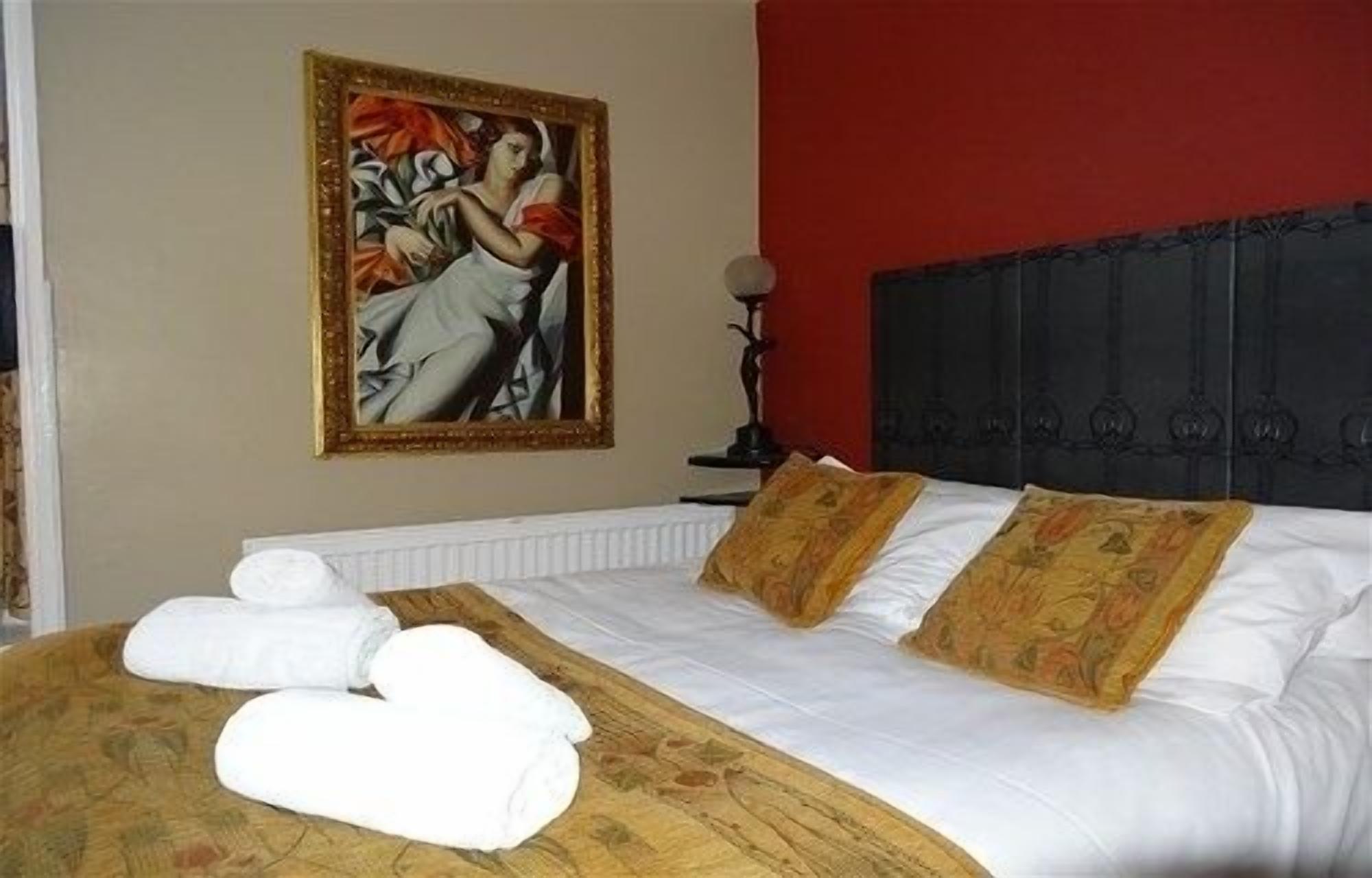 Habitación de hotel con cama, ropa de cama blanca, un cuadro en la pared y una pared de acento roja.