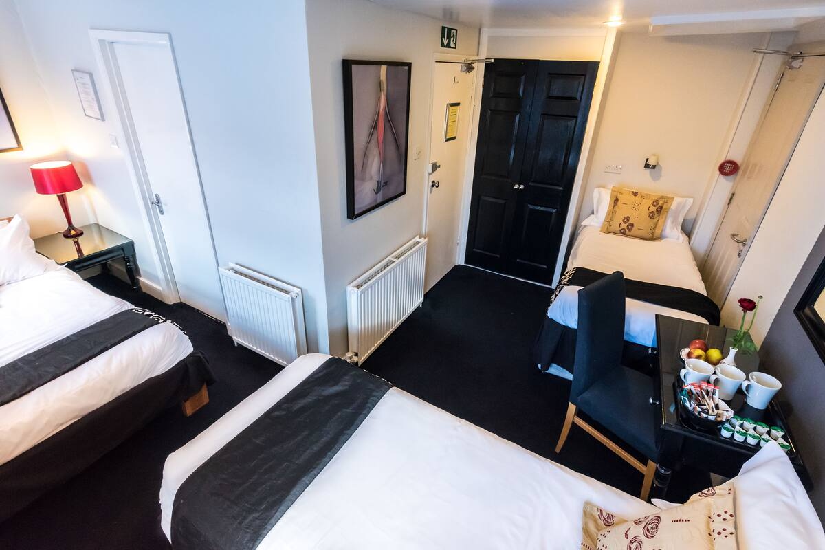 A hotel room with two beds, a desk with a tray of breakfast items, a black chair, and a door leading to another room.