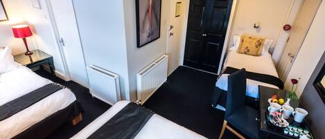 Une chambre d’hôtel avec deux lits, un bureau sur lequel se trouve un plateau avec des articles pour le petit-déjeuner, une chaise noire et une porte donnant sur une autre pièce.