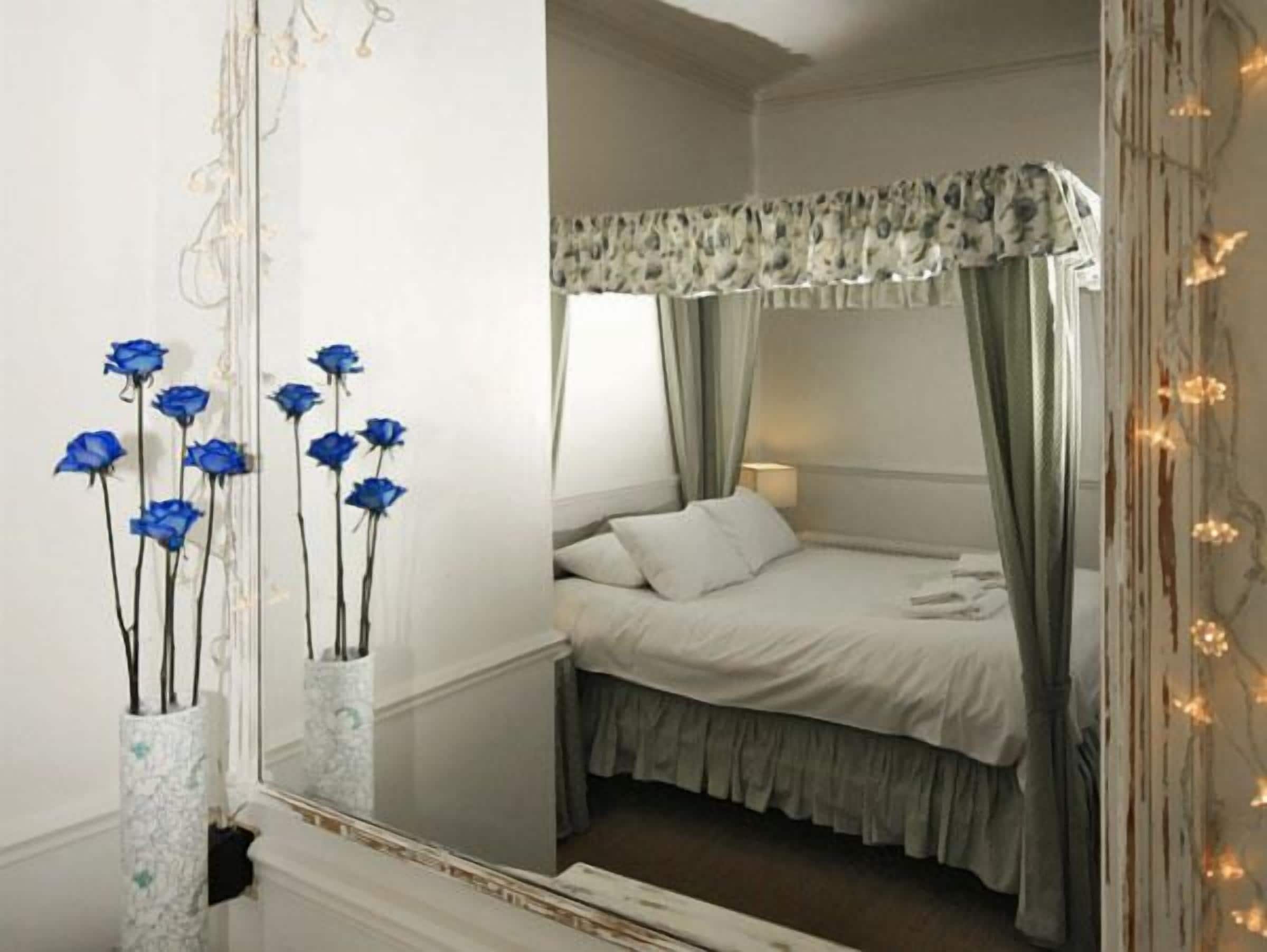 A bedroom with a bed, a mirror, and a vase with blue flowers.