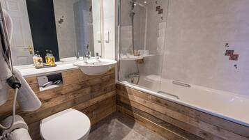 Un baño moderno con tocador de madera, un lavamanos blanco, inodoro y ducha con cerramiento de vidrio.