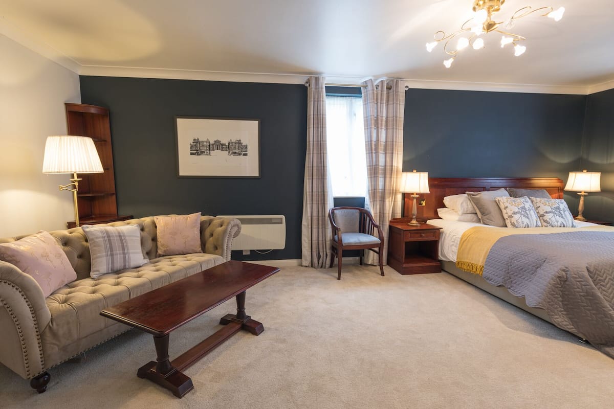 Een hotelkamer met een bed, een slaapbank, een stoel, een tafel en een schilderij aan de muur.
