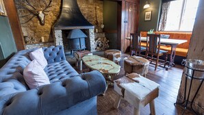 A cozy living room with a stone wall, a fireplace, a blue sofa, and a dining area with wooden chairs and a table. - Duke of Marlborough Hotel (Woodstock)
