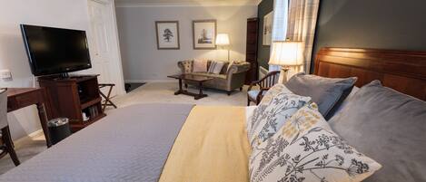 Habitación de hotel con una cama grande, televisión, sofá, mesa de centro y dos lámparas.