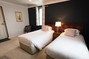 Une chambre d’hôtel avec deux lits, une table de chevet avec une lampe, une chaise, une fenêtre avec des rideaux et un tableau encadré au mur.