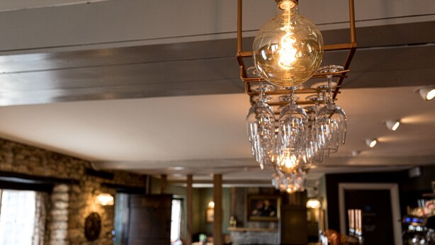 A bar area with a hanging crystal chandelier, stone walls, and a wooden bar counter. - Duke of Marlborough Hotel (Woodstock)