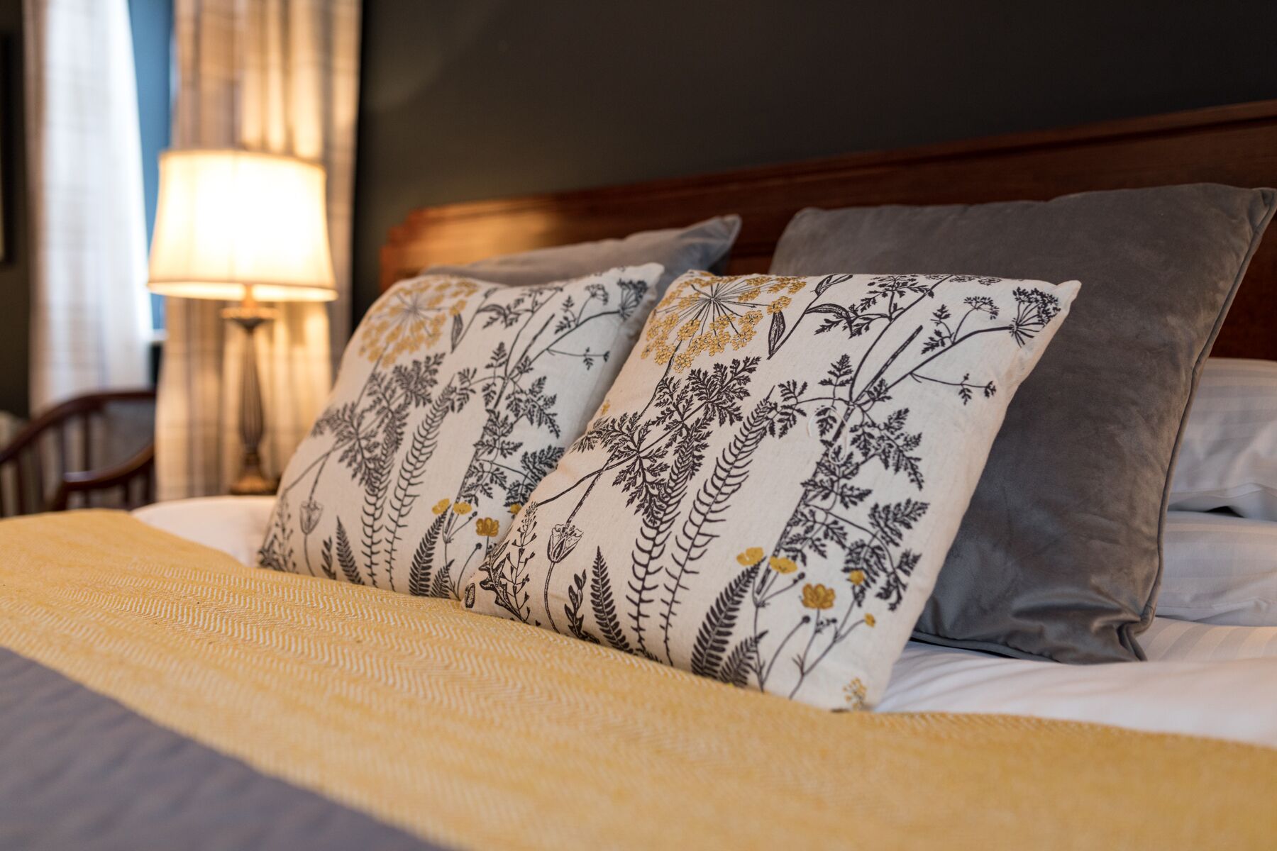 A neatly made bed with a patterned pillow, a bedside lamp, and a wooden headboard.
