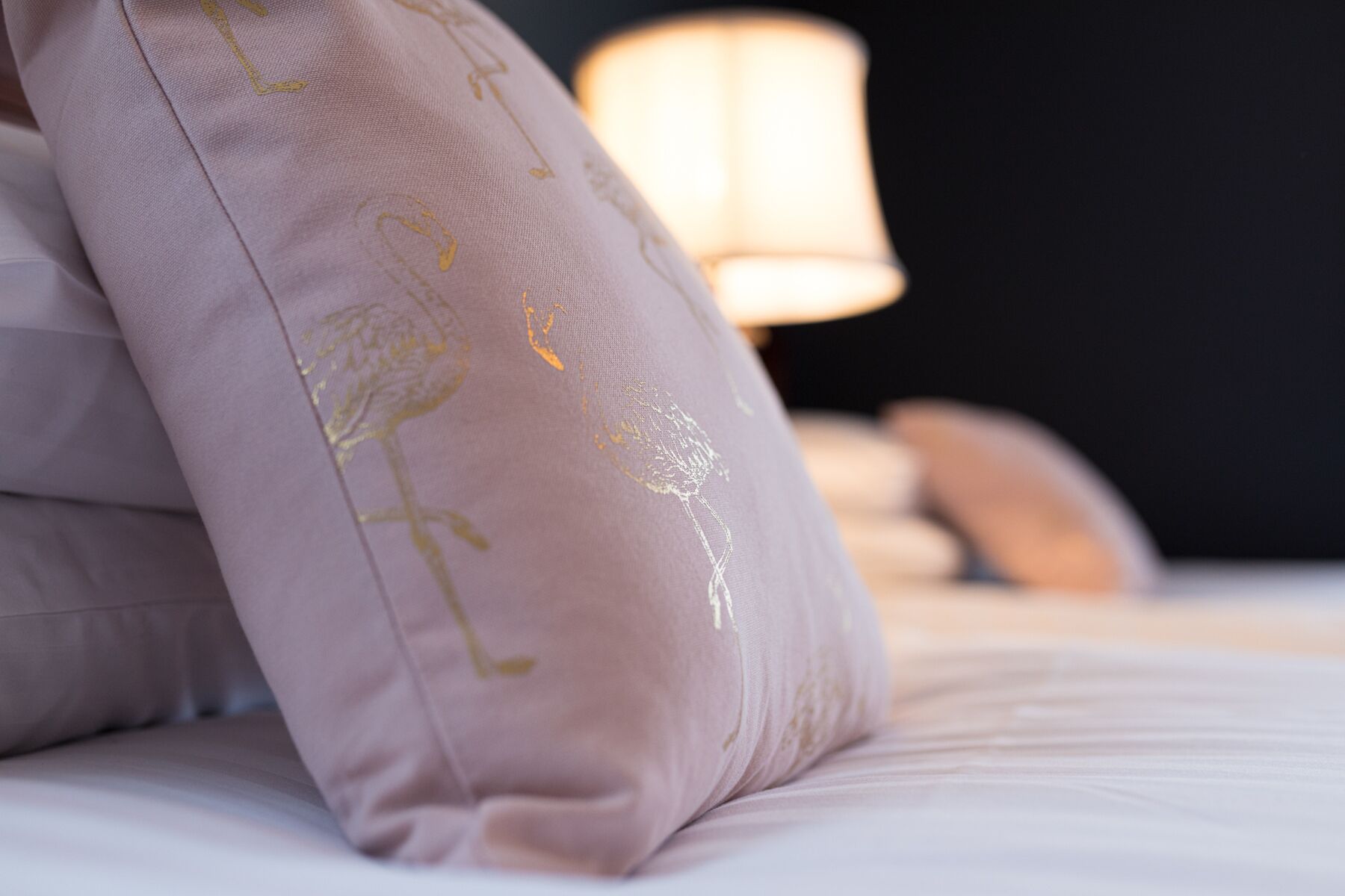 A close-up of a bed with a single pink pillow featuring golden embroidery.