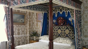 A four-poster bed with a canopy, ornate wallpaper, and a nightstand with a vase of flowers. - The Prince Regent Hotel (Brighton)