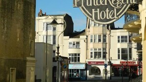 A hotel sign for the Prince Regent Hotel with a classic design, surrounded by buildings with various storefronts. - The Prince Regent Hotel (Brighton)