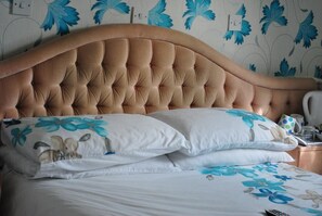A bed with a tufted headboard, white bedding with blue floral patterns, and a nightstand with a kettle and glasses. - The Prince Regent Hotel (Brighton)