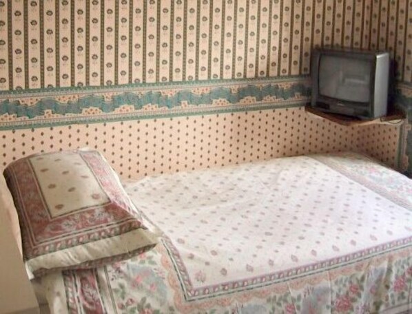 Una habitación con una cama, un televisor sobre un mueble y papel tapiz estampado.