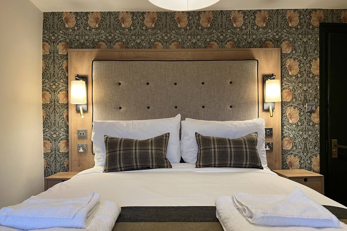 A hotel room with a large bed, two bedside tables, a headboard with a tufted design, and wall-mounted lamps.