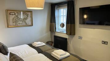 Ein Hotelzimmer mit zwei Betten, einer Karte an der Wand, einem Fenster mit Vorhängen, einem Heizkörper und einem an der Wand befestigten Fernseher.
